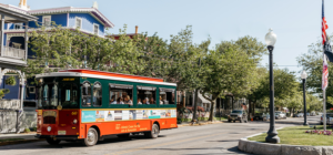 Red and Green Trolley driving down a street filled with victorian homes