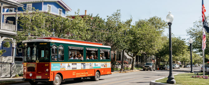 Red and Green Trolley driving down a street filled with victorian homes