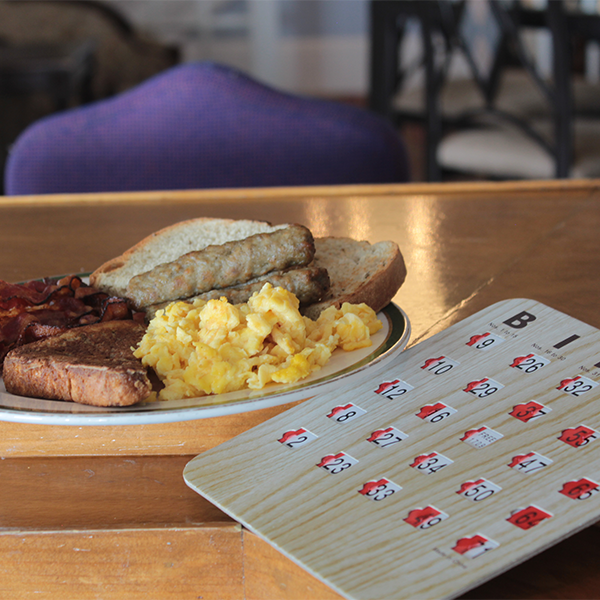 Scrambled eggs, sausage and toast plated on a table next to a bingo card for cape may macs Brunch & Bingo at the beach event.