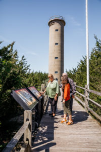 three people looking at informational panels at the world war ii lookout tower in cape may new jersey with the tower in the background
