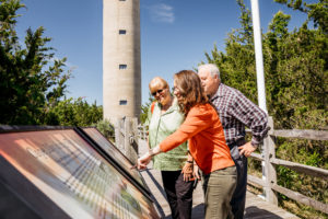 three people looking at informational panels outside the world war ii lookout tower in cape may new jesrey