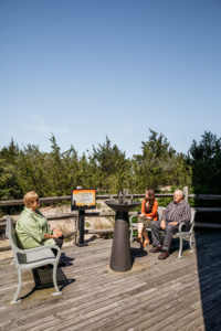 3 people sitting on benches around a memorial called the eternal flame which is placed right outside the world war ii lookout tower in cape may new jersey