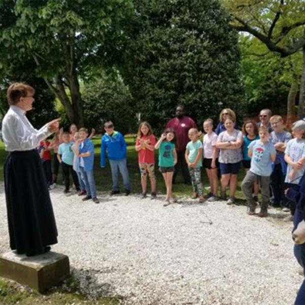 Tour guide dressed in victorian clothing standing outside the physick estate house museum with school children on a field trip