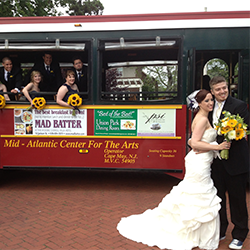 wedding trolley 250×250 bride and groom posing besides a cape may green and red trolley. Bridal party are leaning out the windows.