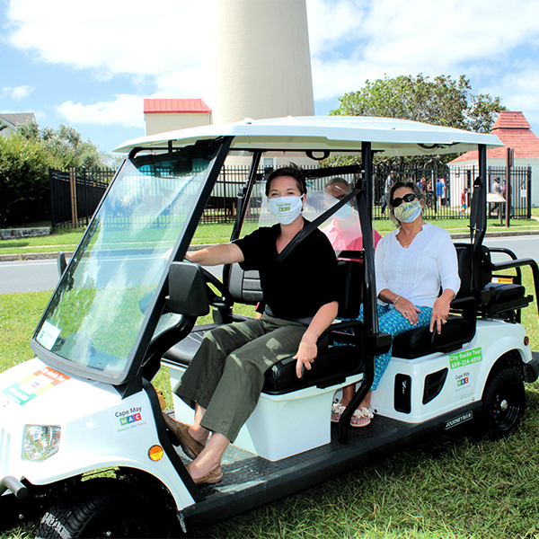 People riding a golf cart in front of the lighthouse with masks on