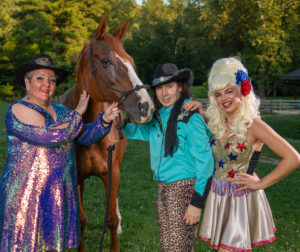 Three people in cowboy outfits standing with a horse