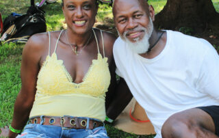 a woman and a man sitting in the grass under a tree