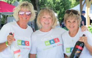 photo of three volunteers at a festival holding bottles of wine