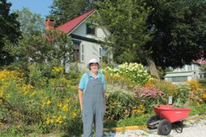 Photo of a woman in overalls standing in front of a garden