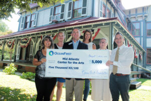 Group of people holding large donation check while standing in front of Physick Estate