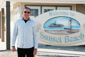 a photo of a man in sunglasses standing next to a sign that says "welcome to sunset beach"