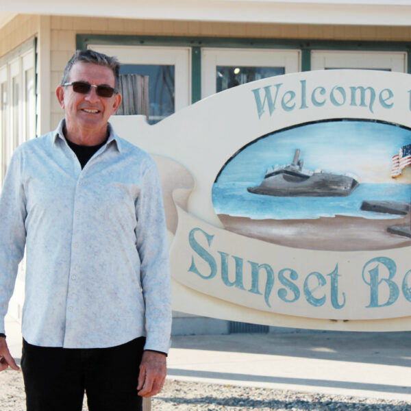 March Larry Hume a photo of a man in sunglasses standing next to a sign that says "welcome to sunset beach"