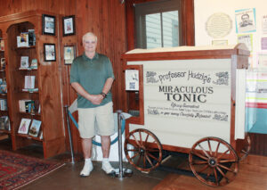 photo of a man standing in front of a small vintage medicine wagon