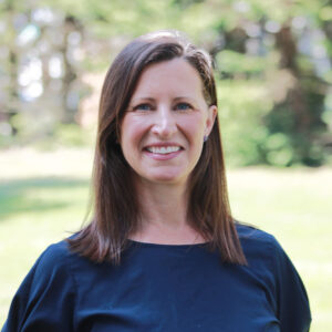 Photo of a woman outside, smiling, with straight brown hair
